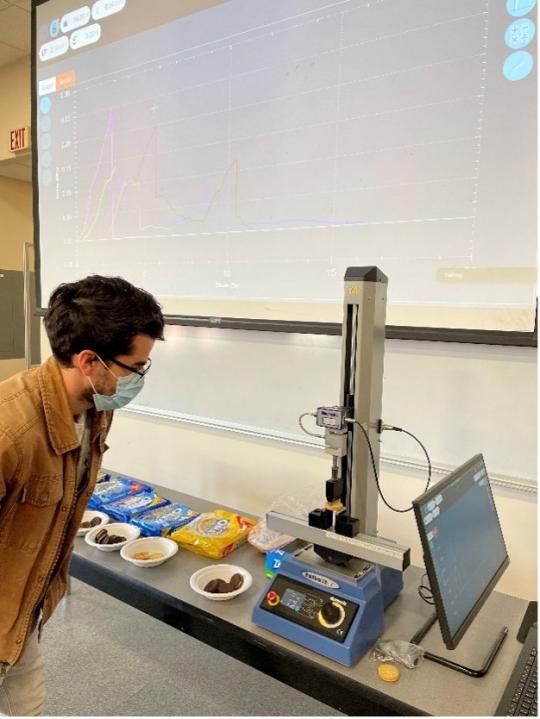在材料科学导论课程的课堂实验中，学生正在观察奥利奥饼干的三点弯曲测试。MultiTest的实时结果被投射到教室里。